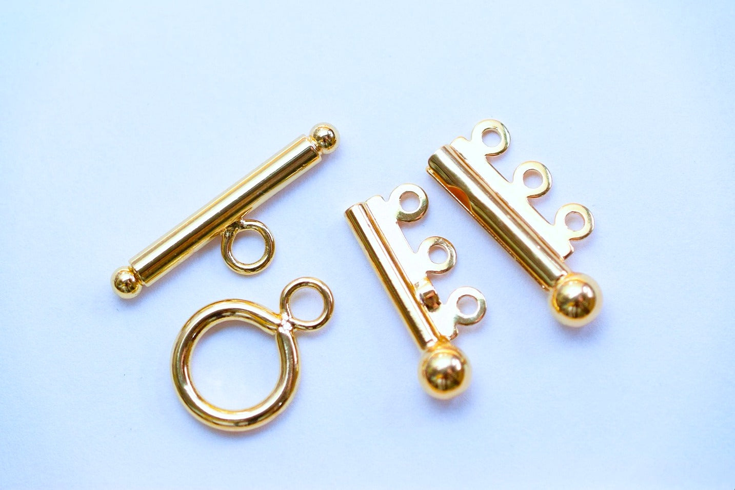 Gold toggle clasp jewelry findings on light blue background.