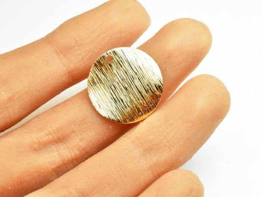 Textured gold round pendant on fingertips.