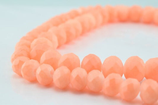 Peach faceted gemstone beads strand on white background.