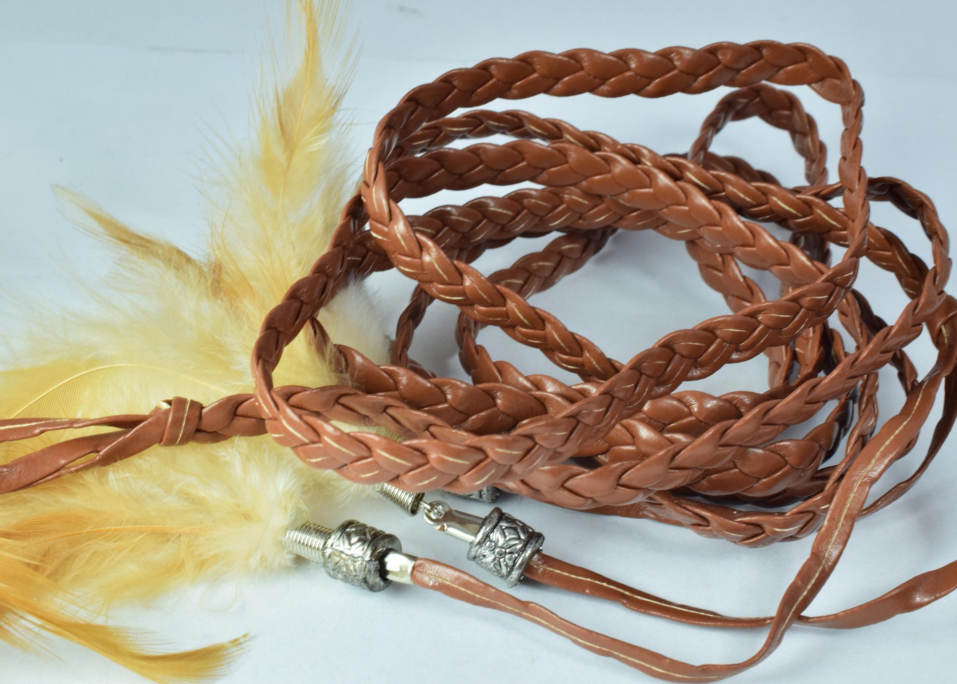 Braided brown leather whip with decorative metal ends and yellow feathers.