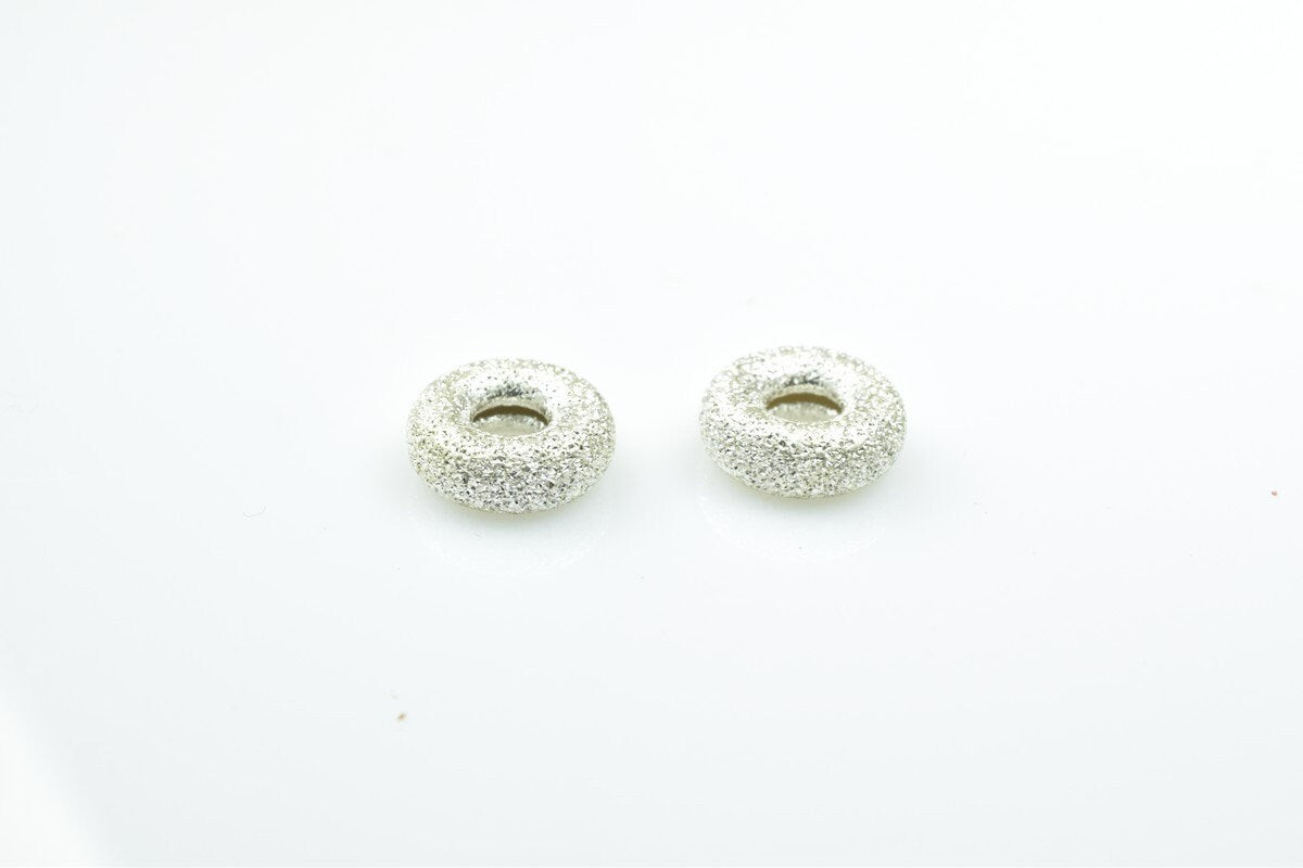 Silver textured donut-shaped beads on white background.