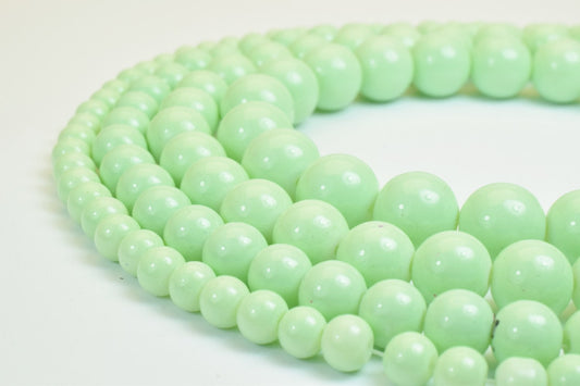 Pale green bead necklace arranged in loops on a white background.