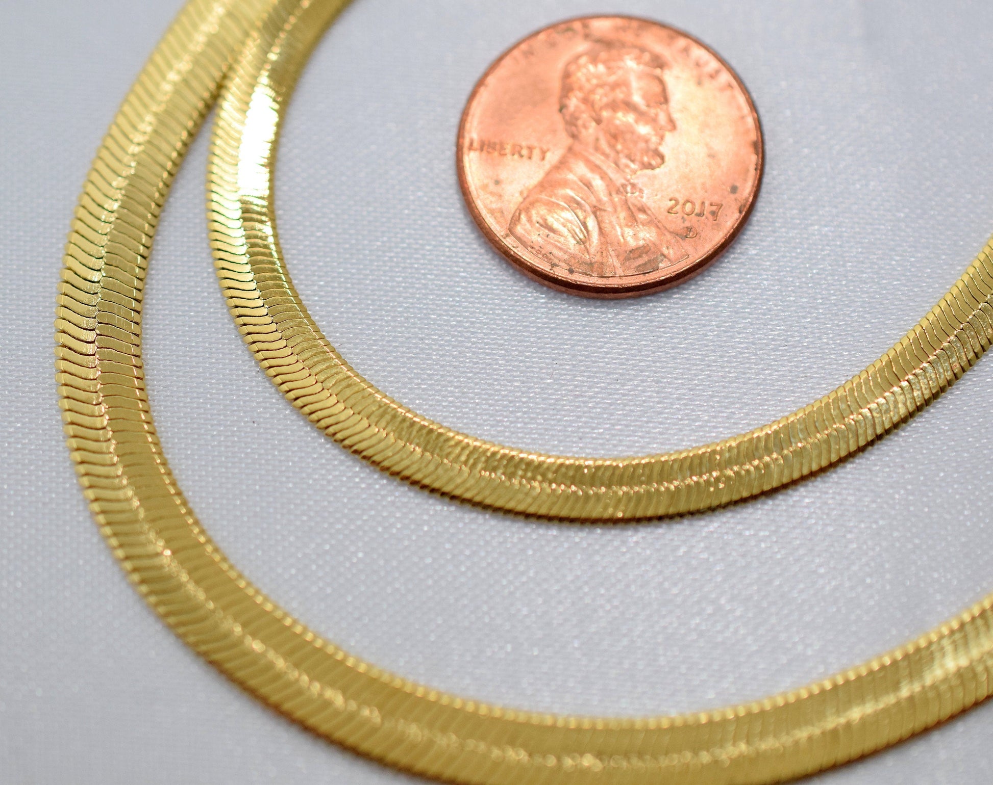 Gold herringbone chain necklace next to a penny for size comparison.