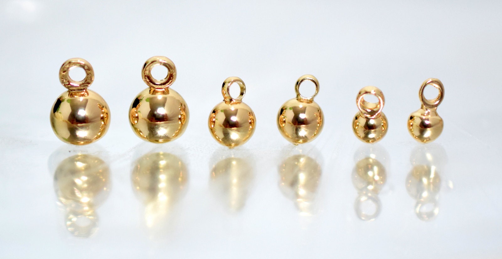 Gold round pendant charms in assorted sizes on white background.