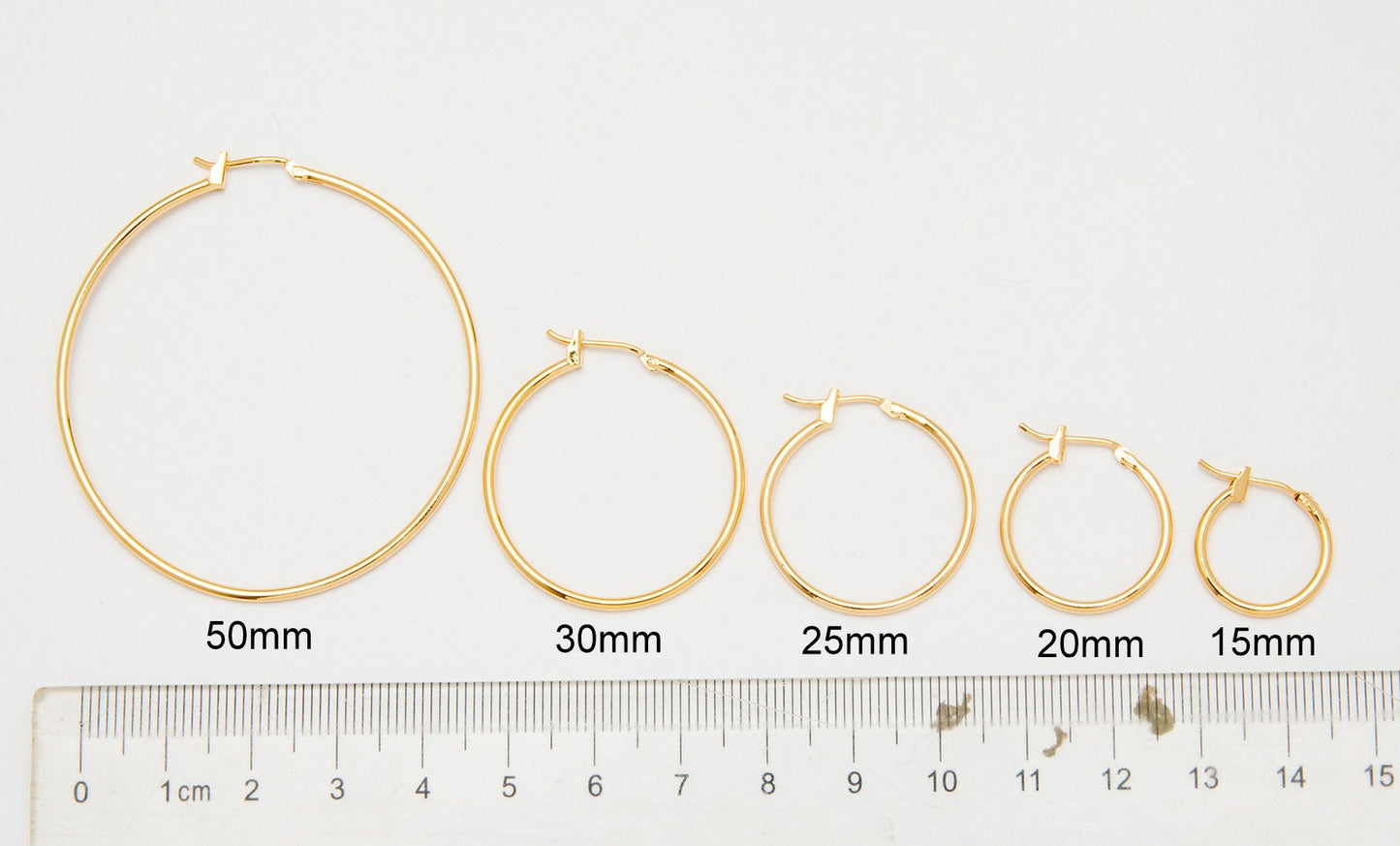 Gold hoop earrings in various sizes with ruler for scale.