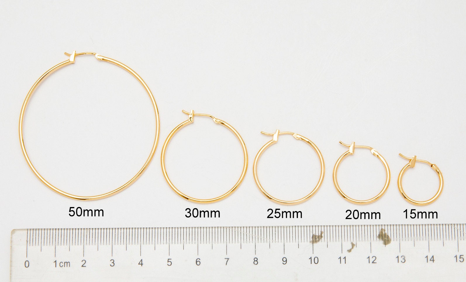 Gold hoop earrings in various sizes with ruler for scale.