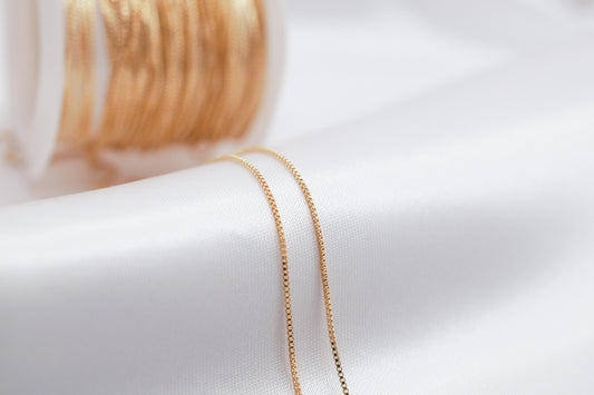 Gold box chain necklace on white satin background.