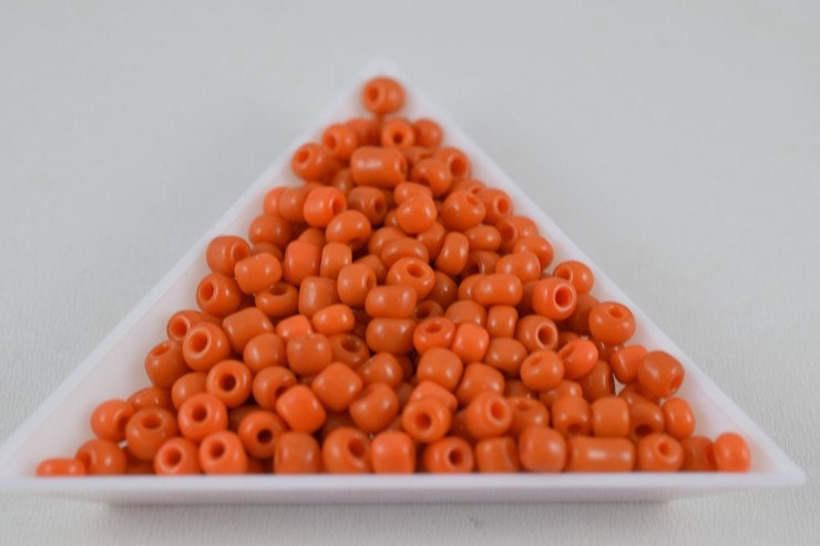 Orange seed beads in triangular white dish.