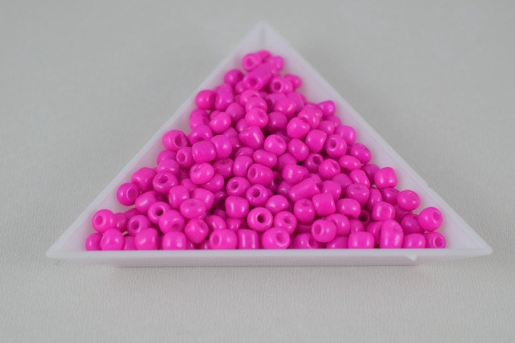 Triangular white tray filled with pink seed beads on gray background.