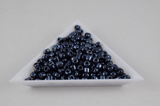 Black glass seed beads in a triangular container.